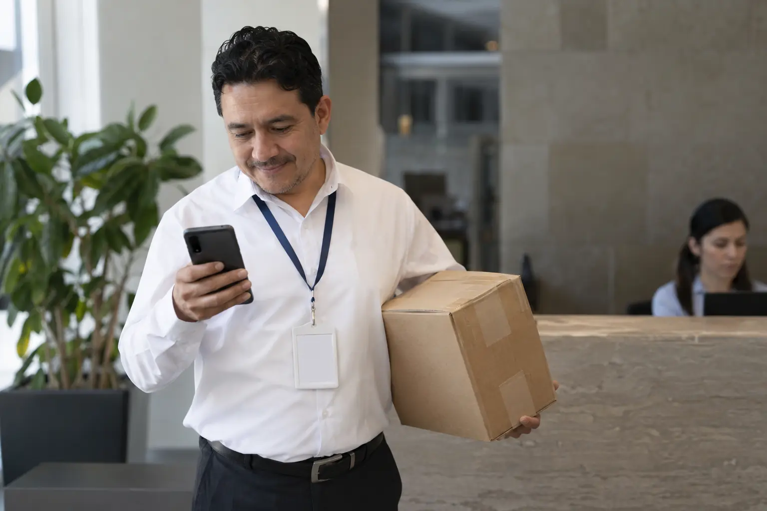 Un trabajador recibe un paquete en la recepción de su oficina mientras revisa su celular